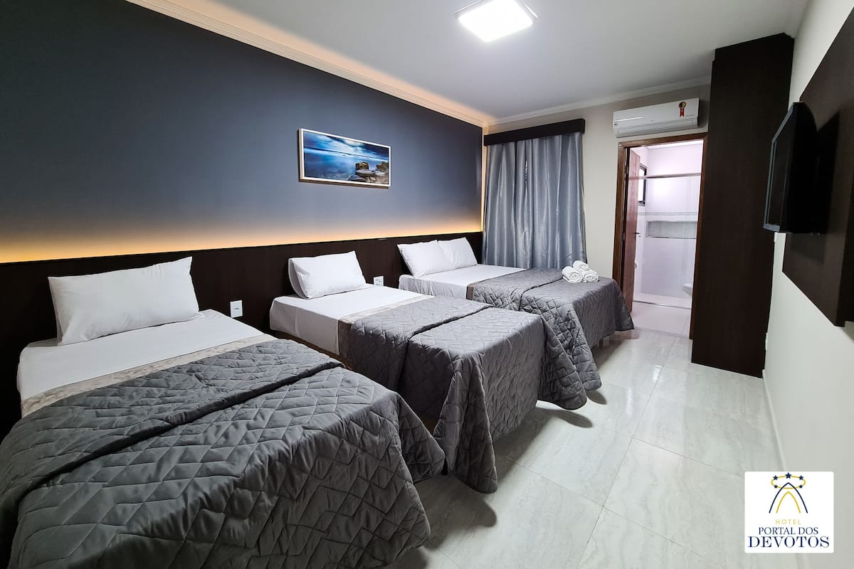 A hotel room with three beds, a painting on the wall, an air conditioning unit, and a television on the wall.
