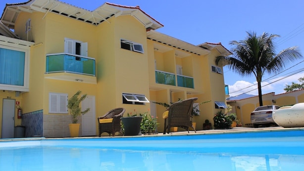 A yellow building with a swimming pool, balconies, and potted plants. - Pousada Cabore (Paraty)