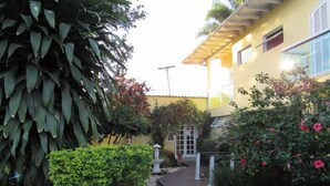 A pathway leading to a building with a yellow facade, surrounded by lush greenery and flowering plants. - Pousada Cabore (Paraty)