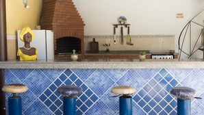 A kitchen with a brick oven, a refrigerator, and a bar area with stools. - Pousada Cabore (Paraty)