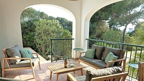 A patio with wooden furniture, including a sofa and chairs, and a small table with a bottle and glasses. - Villa Persephone (Binibequer)