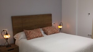 A bedroom with a wooden headboard, two bedside lamps, a bed with white bedding, and a nightstand with drawers. - 108 - Paraje de Los Lances (Tarifa)
