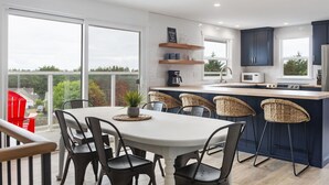 A modern kitchen with a large island, dark cabinets, and a view through large windows. - HOT TUB! Sunset Views. Walk to Beach. Pet Friendly. Sleeps 10! (Westport)