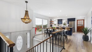 A modern kitchen with dark cabinets, a stainless steel refrigerator, and a dining area with wicker chairs. - HOT TUB! Sunset Views. Walk to Beach. Pet Friendly. Sleeps 10! (Westport)