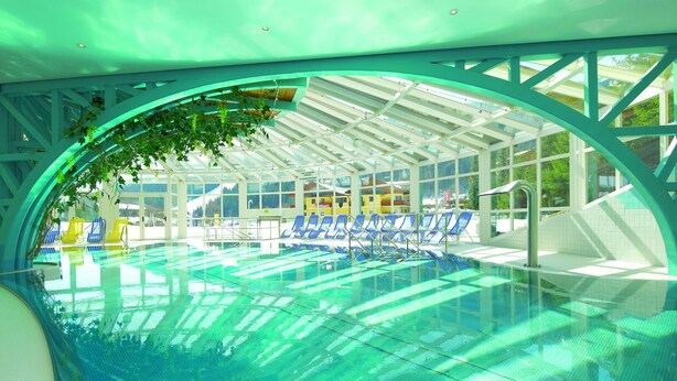 Una piscina interior con paredes de vidrio transparente, sillones reclinables azules y una estructura de techo.