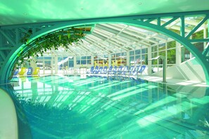 A covered swimming pool with blue chairs and a glass ceiling. - A charming little vacation home in a central location (Filzmoos)
