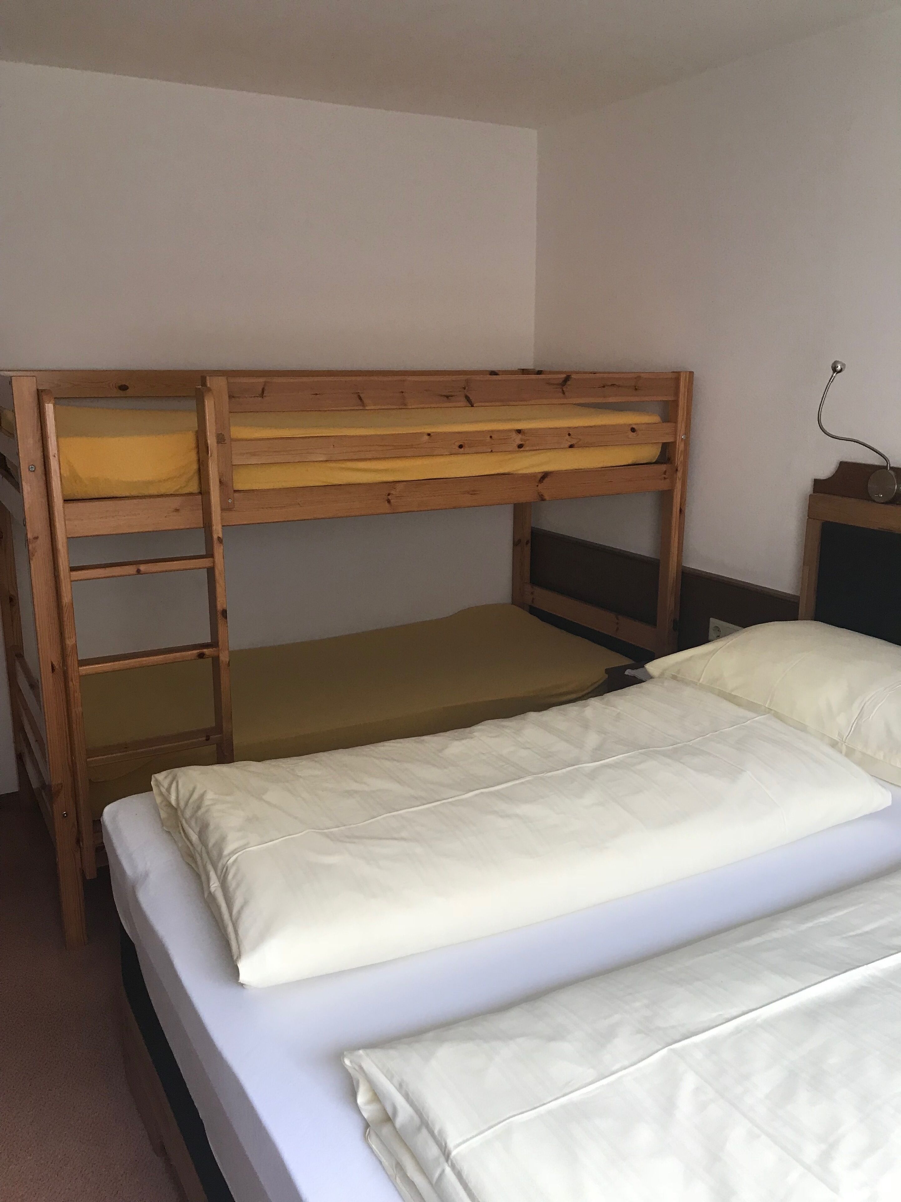 Een stapelbed met houten frame, een onderste bed met een gele matras en een bovenste bed met een witte matras.
