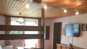 Una habitación acogedora con techo de madera, una mesa de comedor con sillas, un televisor montado en la pared y una ventana con cortinas.