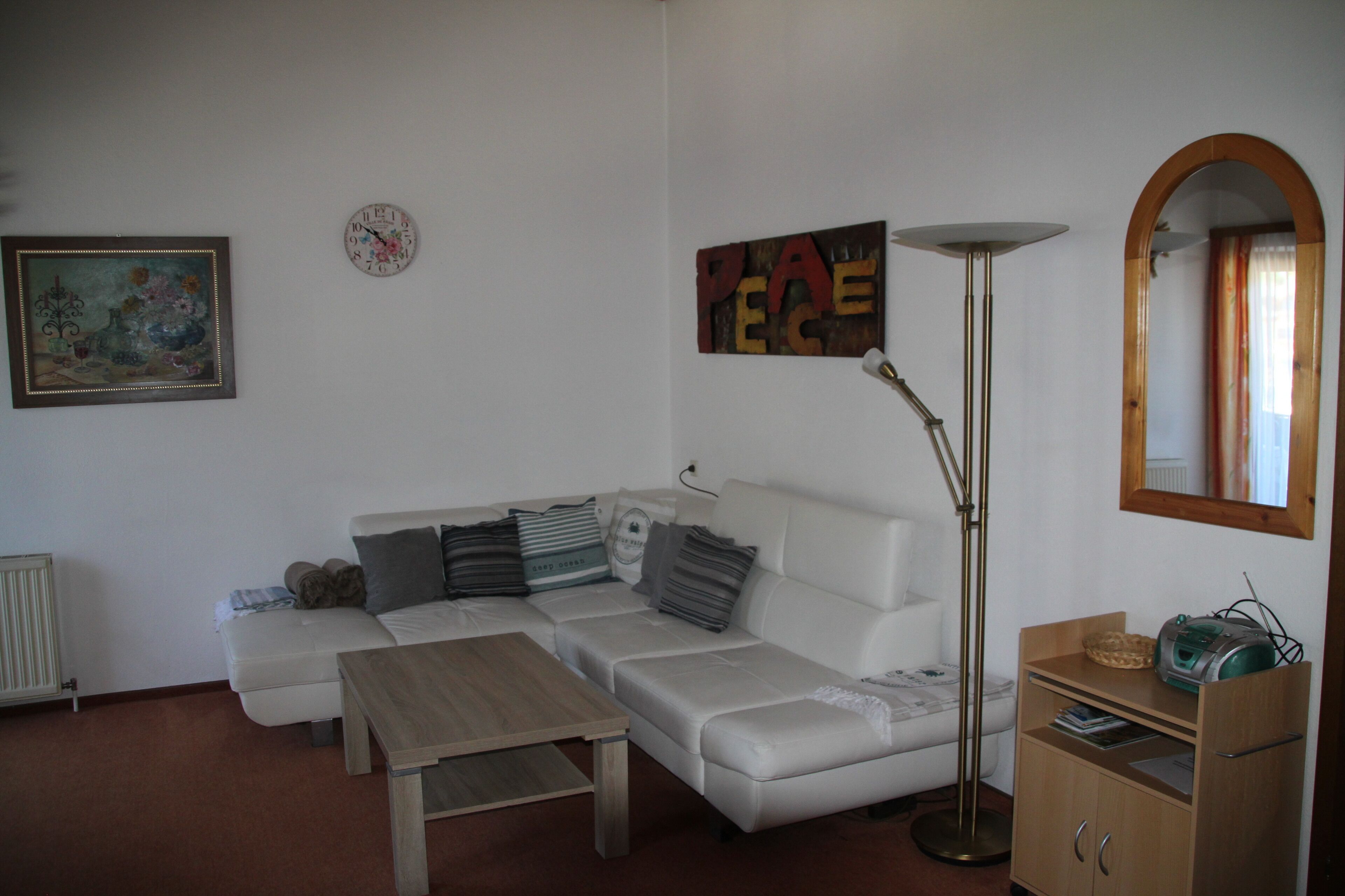 Un salon avec un canapé blanc, une table basse en bois, un lampadaire, une bibliothèque et un tableau accroché au mur.