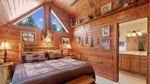 Un dormitorio rústico de madera con una cama grande, dos lámparas de noche, un tragaluz y vistas al exterior.