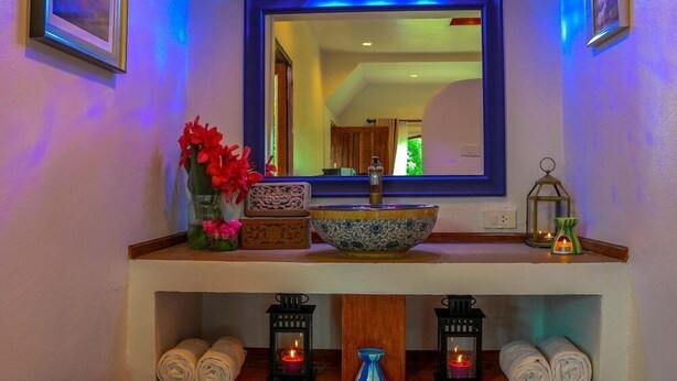 Uma toucador de banheiro com um espelho grande, uma cuba e uma prateleira com toalhas e velas.