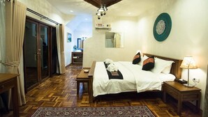 Quarto com piso de madeira, cama com roupa de cama branca, mesa de cabeceira com abajur e luminária no teto.