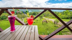 Duas bebidas sobre uma mesa de madeira, com vista panorâmica para uma paisagem verde e montanhas ao fundo.