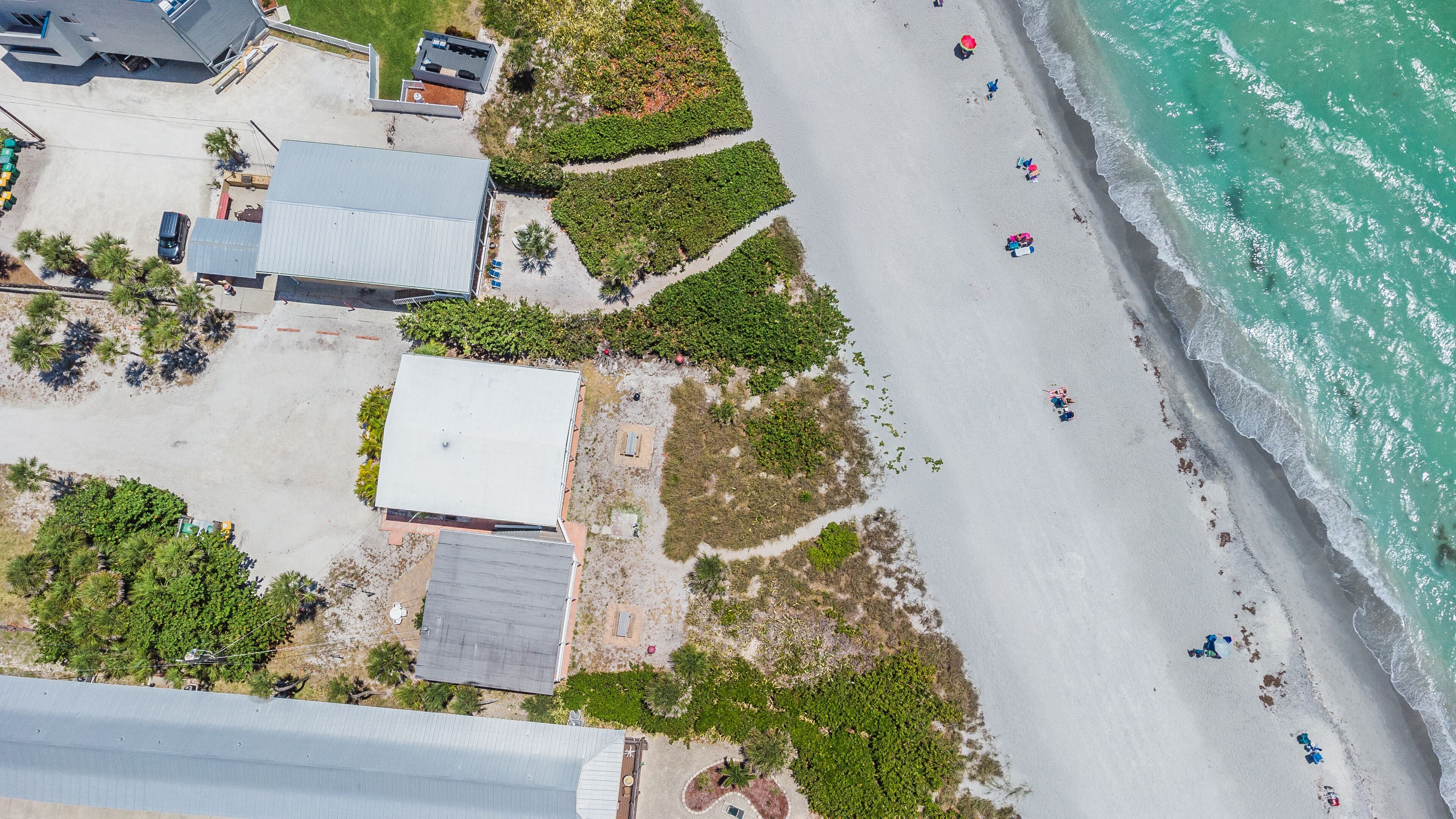 Vue aérienne d’une propriété située sur la côte, avec une plage, un espace de stationnement et plusieurs bâtiments.