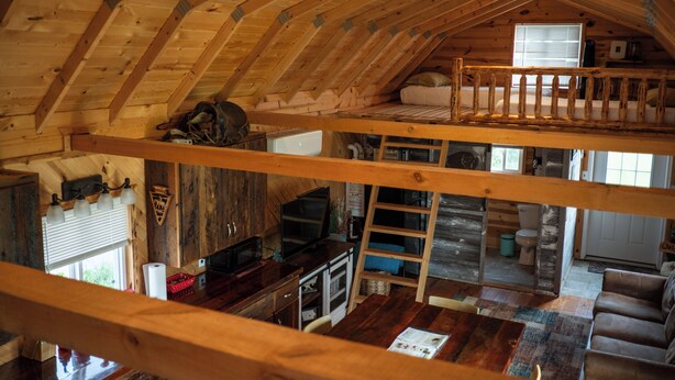 A loft-style room with a wooden ceiling, a bunk bed, a desk, and a kitchen area.
