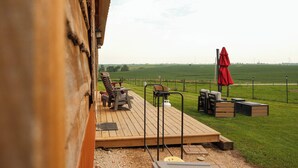 A deck with outdoor seating, a red umbrella, and a view of a green field.
