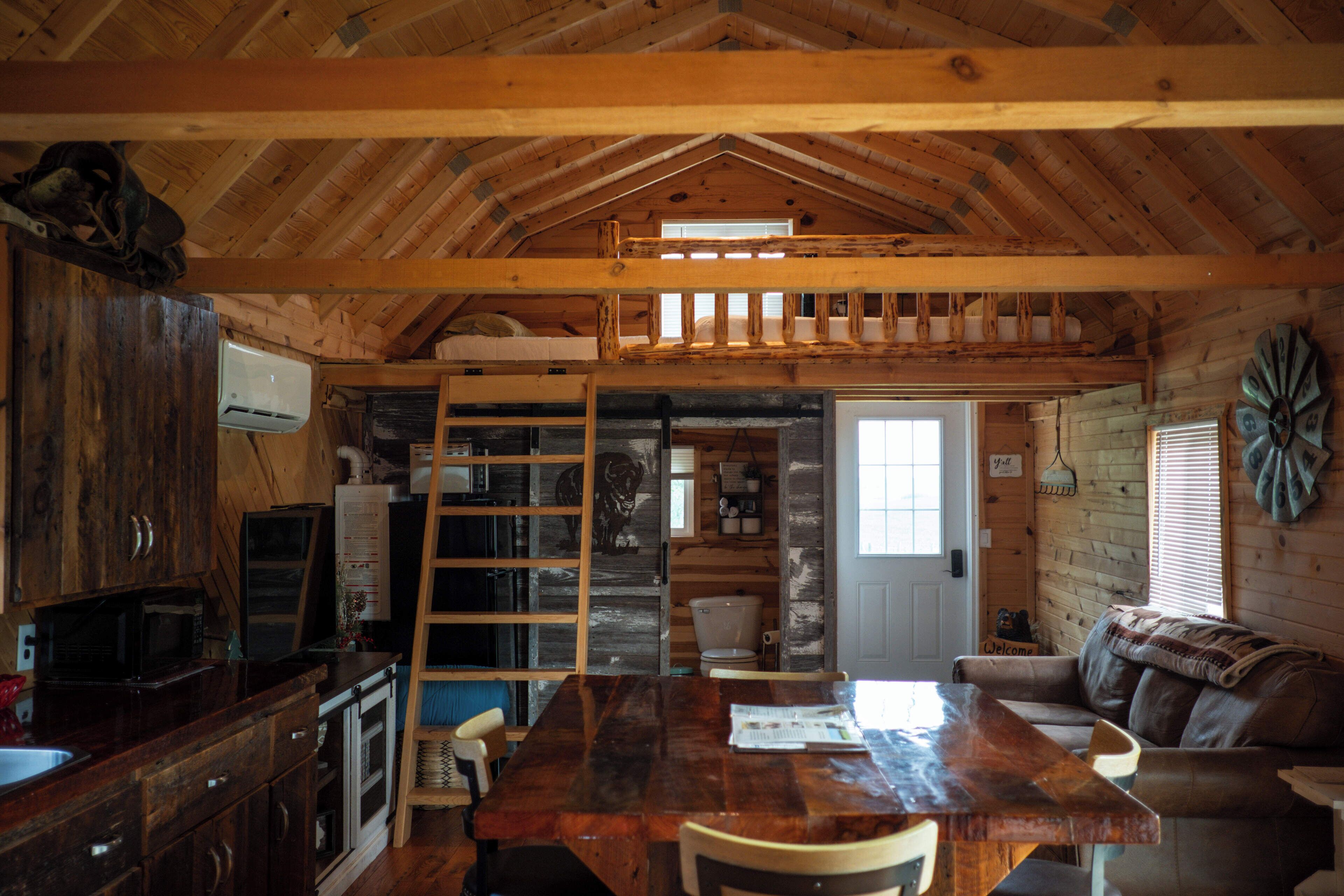 L’intérieur d’un chalet rustique est aménagé avec une table à manger en bois, un canapé et une échelle menant à une mezzanine.