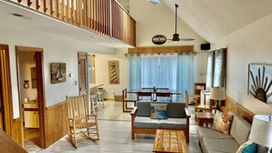 A spacious living area with a high ceiling, wooden furniture, and a dining area with a view of the outdoors. - Avon NC OBX Dog-Friendly Home  - Short walk to the Beach or Sound - PARK PLACE (Avon)
