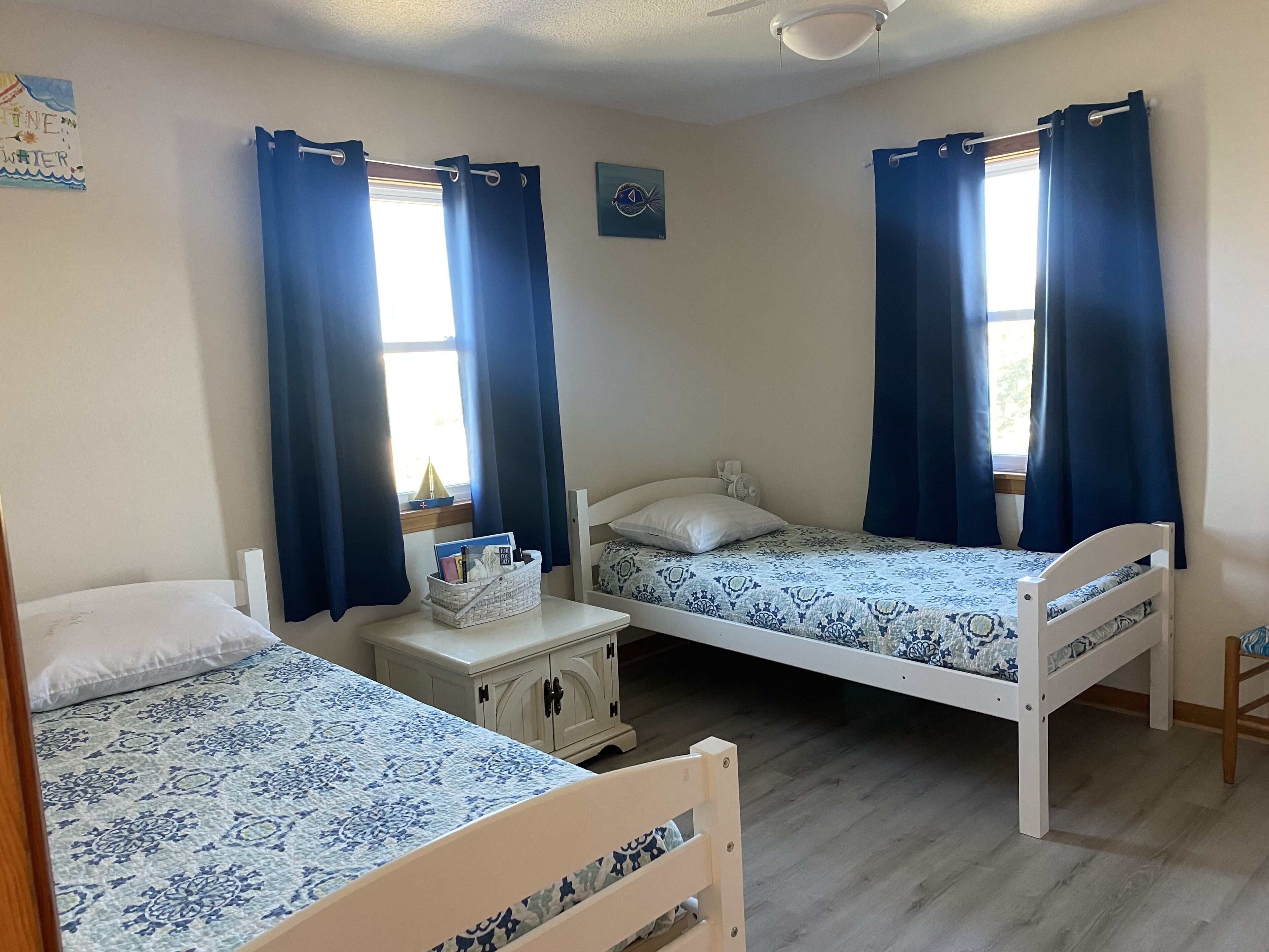 A room with two single beds, a small bedside table with a lamp, and a window with curtains.
