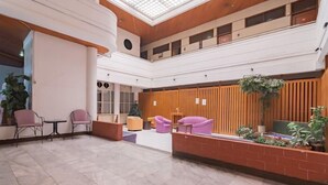 A spacious lobby with a high ceiling, a reception desk, and seating areas with chairs and tables. - RedDoorz near Hyperpoint Pasteur 2 (Bandung)