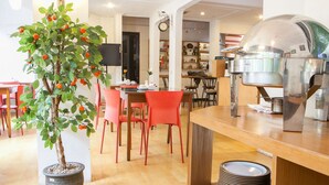 A dining area with a potted tree, red chairs, a wooden table, and a coffee machine. - RedDoorz near Hyperpoint Pasteur 2 (Bandung)