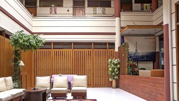 A spacious lobby with a high ceiling, a seating area with sofas and armchairs, a patterned rug, and a large poster of the Eiffel Tower. - RedDoorz near Hyperpoint Pasteur 2 (Bandung)