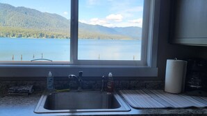 A kitchen with a large window offering a view of a lake and mountains.