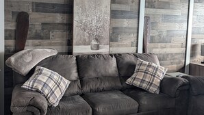 A dark leather sofa with plaid cushions, a framed floral artwork, and a wooden wall panel.