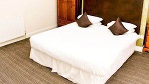 Una cama bien hecha con ropa blanca y dos almohadas marrones, un armario de madera y un radiador en la pared.
