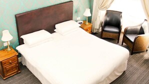 Una habitación de hotel con una cama, dos mesitas de noche con lámparas, una silla y un ventanal con cortinas.