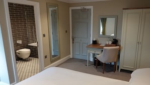 Habitación de hotel con una cama grande, un escritorio con silla, baño con inodoro y espejo, y un armario.