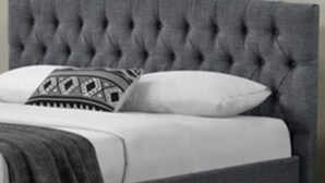 Una cama con cabecera capitonada, ropa de cama blanca y almohadas estampadas.
