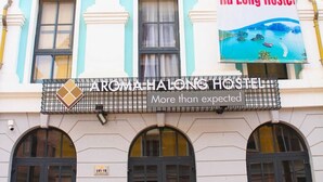 Een gebouw met een bord voor Aroma Halong Hostel, inclusief een gastvrije banner en een pittoresk beeld van een kustgebied.