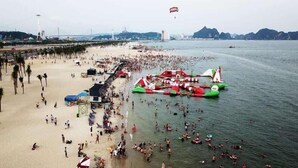 Een druk strand met opblaasbare waterattracties en een pier op de achtergrond.