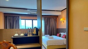 A hotel room with a bed, a desk with a coffee maker, and a view of the outdoors through the window.