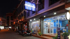 A building with a sign for 'DIYANA RESIDENCE' and a 'ROOM FOR RENT' section. There are motorcycles parked outside, and a person is sitting on a chair near the entrance. - Diyana Residence (Pattaya)