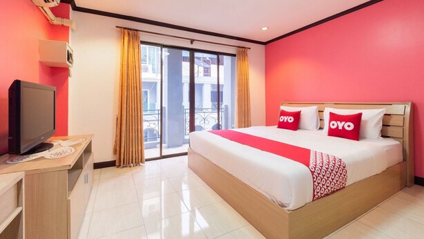 A hotel room with a large bed, a television on a wooden table, and a sliding glass door to the outside. - Diyana Residence (Pattaya)