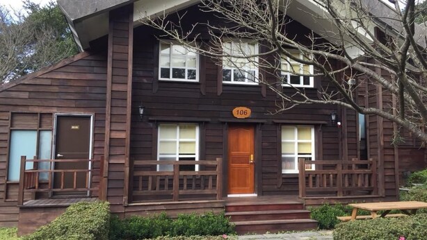 A two-story wooden cabin with a front porch, a wooden door, and a number '106' sign. - Yangmingshan Jing Shan Recreation Area (Taipei)