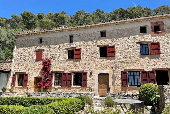 A stone building with red shutters, a wooden door, and a small garden area. - Authentic Mas in the middle of a magnificent property. Impressive view. (Cabris)