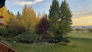 A grassy outdoor area with trees, a stone wall, and a wooden deck. - Welcome to CoCo Ranch Mtn Stay – Your Private Teton Valley Escape! (Victor)