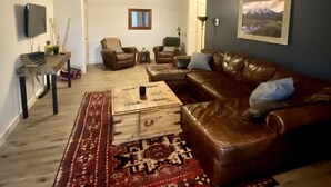 A living room with a brown leather sofa, a wooden coffee table, a patterned rug, and a television on the wall. - Welcome to CoCo Ranch Mtn Stay – Your Private Teton Valley Escape! (Victor)