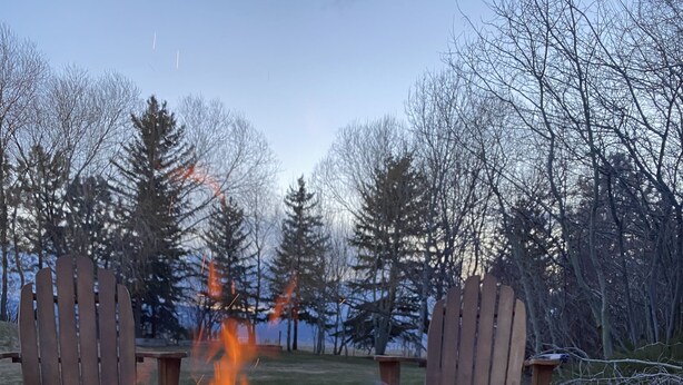 A campfire with two Adirondack chairs facing it, set in a grassy outdoor area with trees in the background. - Welcome to CoCo Ranch Mtn Stay – Your Private Teton Valley Escape! (Victor)