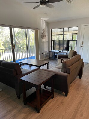 Relax in a spacious living area with a sofa, coffee table, and flat-screen TV, plus a sliding glass door to an outdoor balcony.
