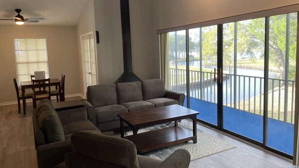 A spacious living room with a large window, a ceiling fan, and a dining area with a table and chairs. - Manatee Manor. Waterfront, dock, stilted home. Renovated June '23.  (Homosassa)