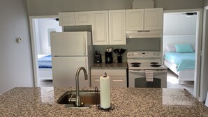 A kitchen with granite countertops, a stainless steel sink, a white refrigerator, a stove, and white cabinets. - Manatee Manor. Waterfront, dock, stilted home. Renovated June '23.  (Homosassa)