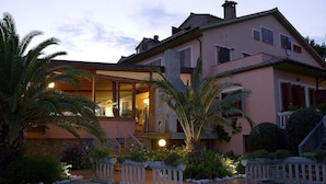 A two-story house with a balcony, surrounded by palm trees and a stone pathway. - Agrihotel Elisabetta (Cecina)