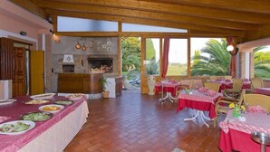 A spacious dining area with a long table set for a meal, a fireplace, and a view of the outdoors. - Agrihotel Elisabetta (Cecina)