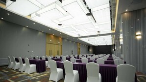 Un salón de conferencias con filas de mesas y sillas, un techo alto con tragaluces y suelo alfombrado.