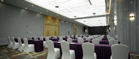 A conference room with rows of tables and chairs, a high ceiling with skylights, and a carpeted floor.