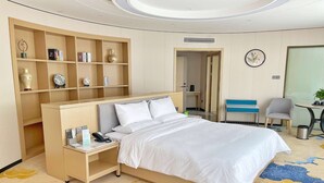 Una habitación de hotel con una cama, un escritorio con teléfono, una estantería y una silla.